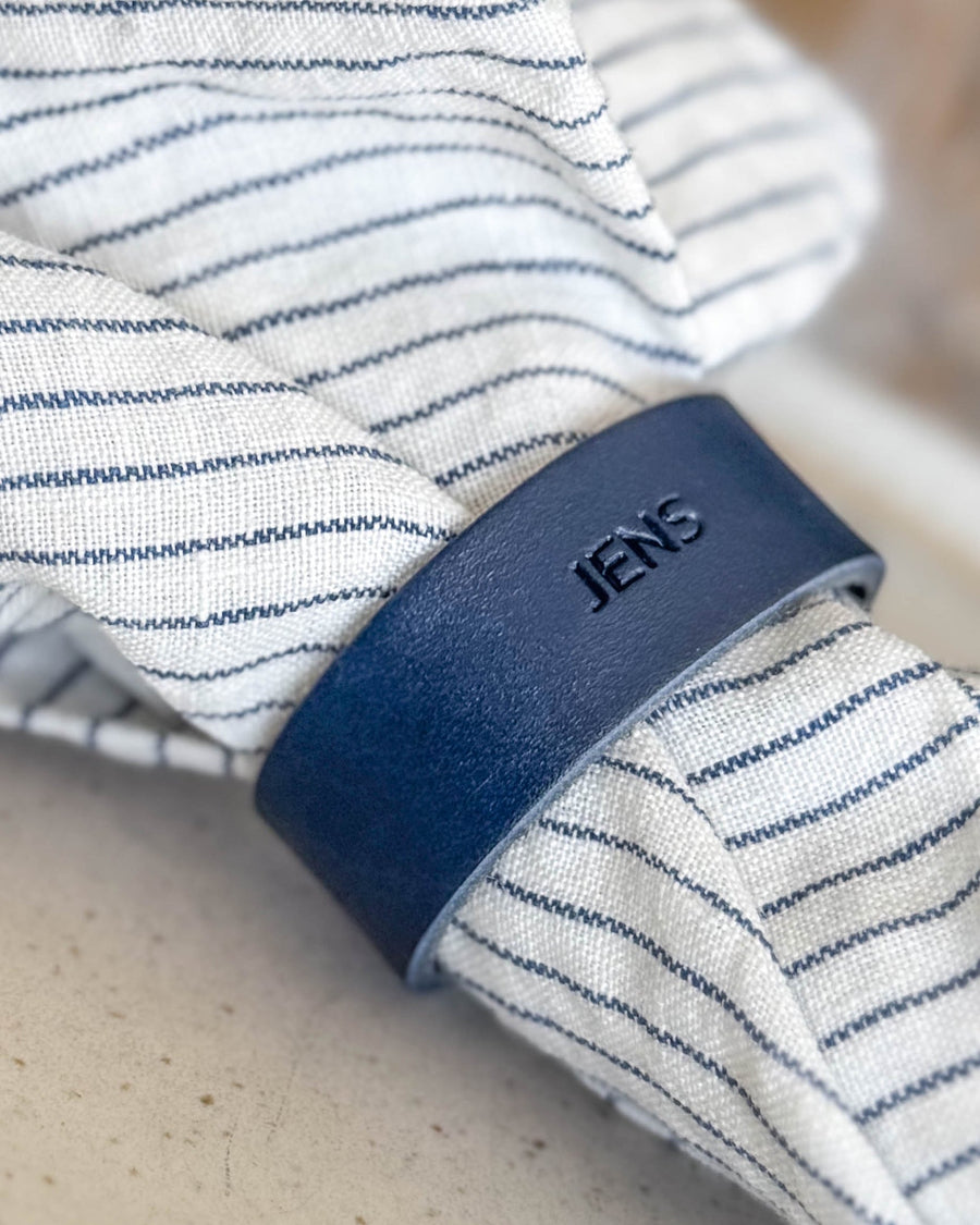 KNOT napkin ring place card in navy blue leather with the name "Jens" engraved around a striped linen napkin