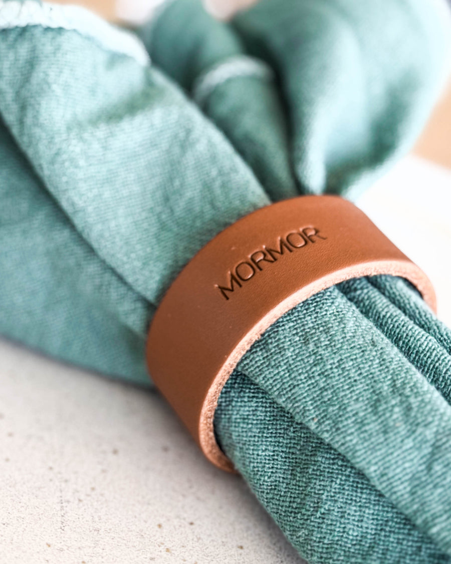 KNOT napkin ring in cognac leather with the engraving "Mormor" around a green cloth napkin
