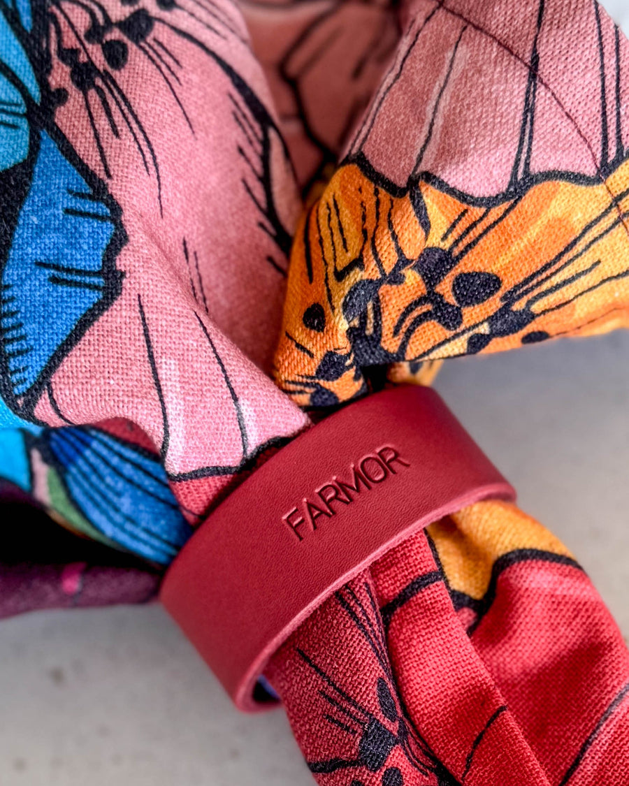 KNOT napkin ring place card in red leather with the engraving "Farmor" around a colourful floral napkin