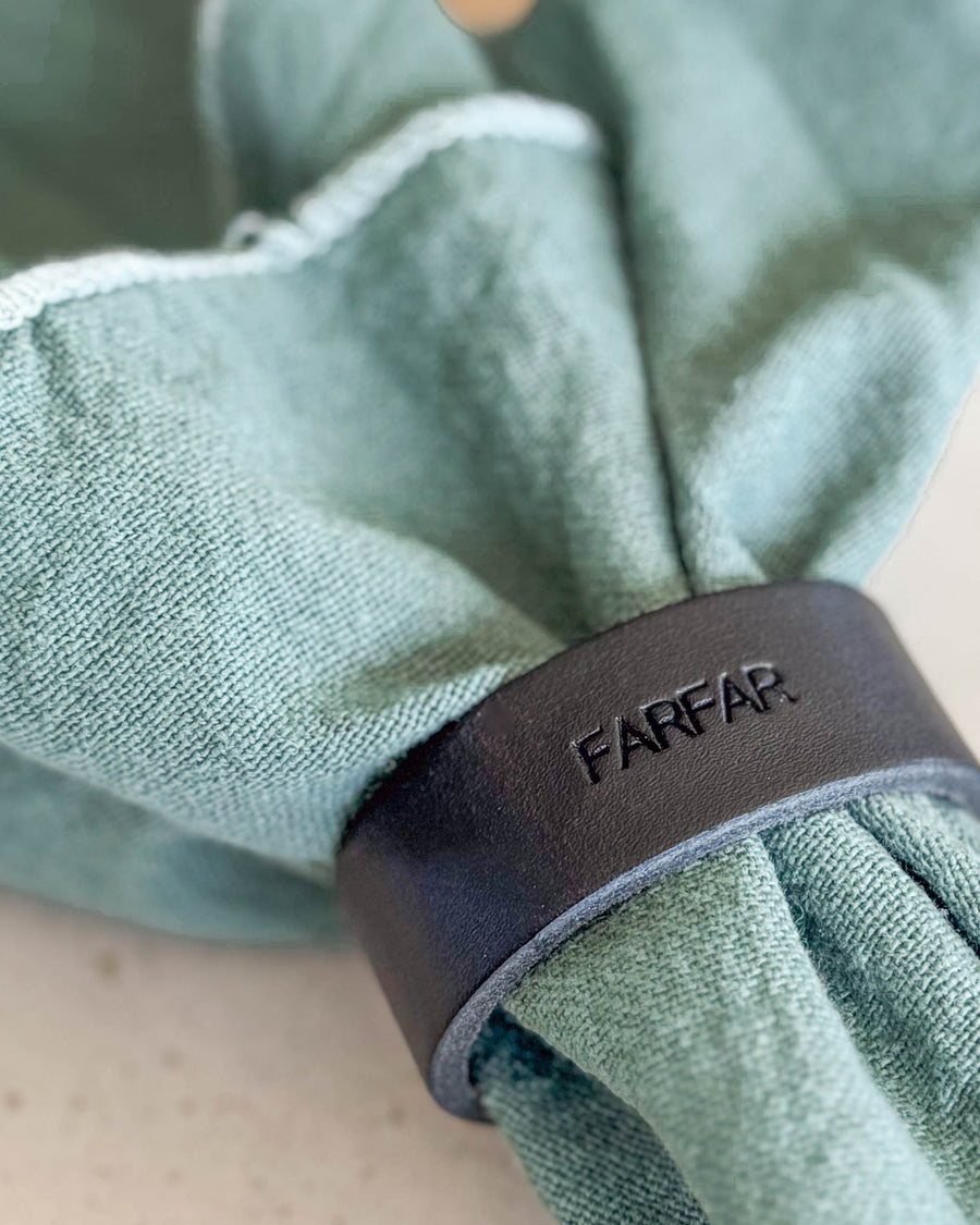 KNOT napkin ring place card in black leather with the engraving "Farfar" around a light green cloth napkin
