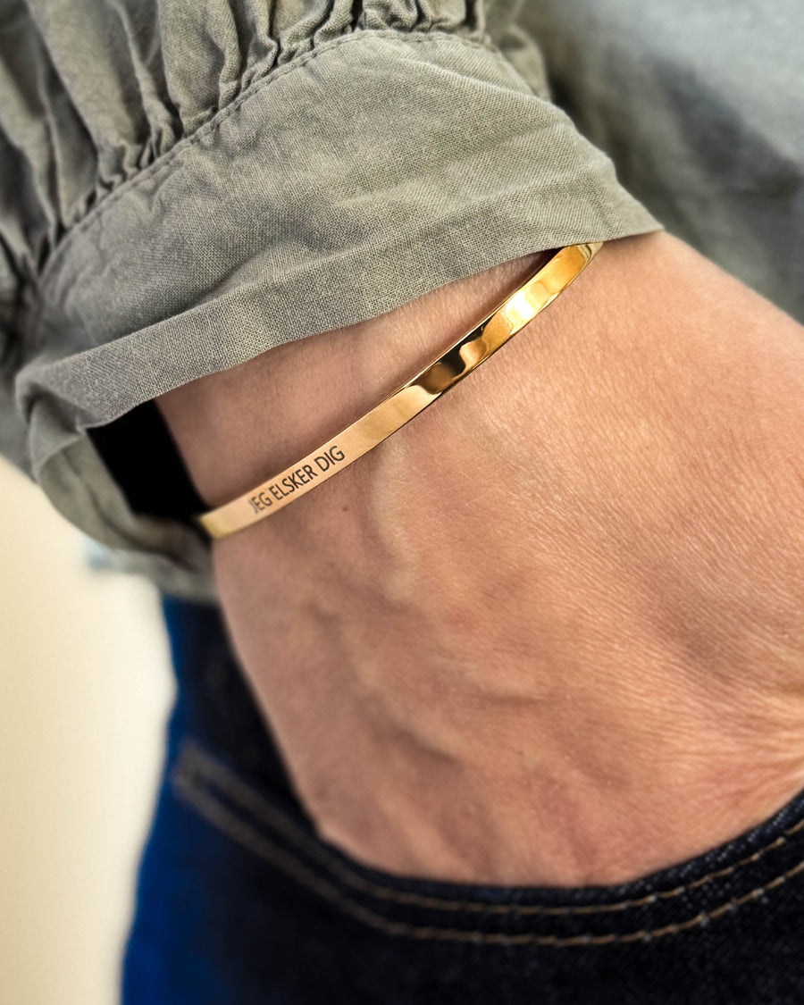 VENUS bracelet in gold-plated stainless steel with the engraving "Jeg elsker dig" on the wrist, hand in dark jeans pocket