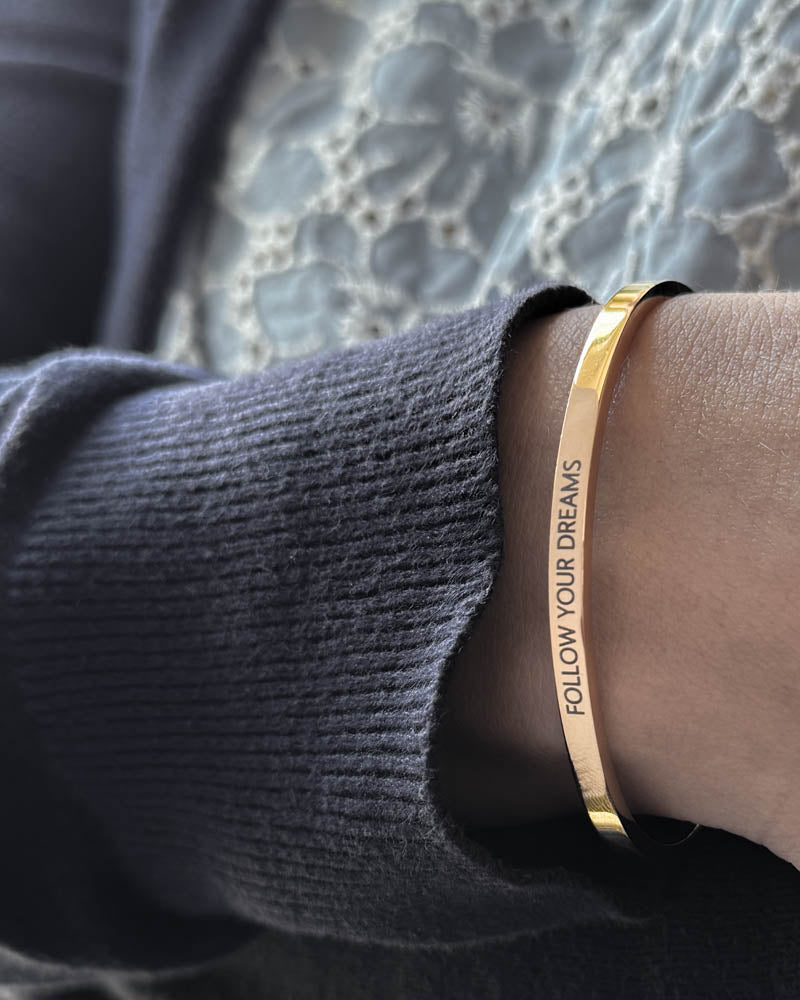 VENUS bracelet in gold-plated stainless steel with the engraving "Follow your dreams" in capitals, worn with navy knit and lace blouse