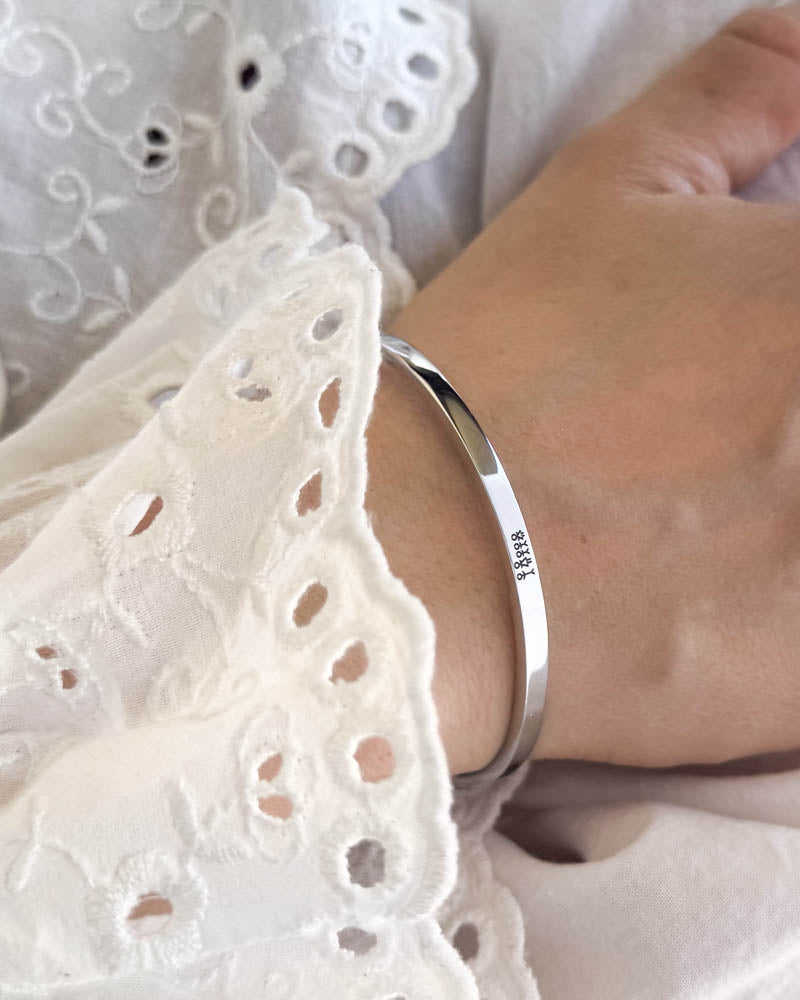 VENUS STICK bracelet in silver-coloured stainless steel with engraved matchstick family, worn with a white embroidered blouse