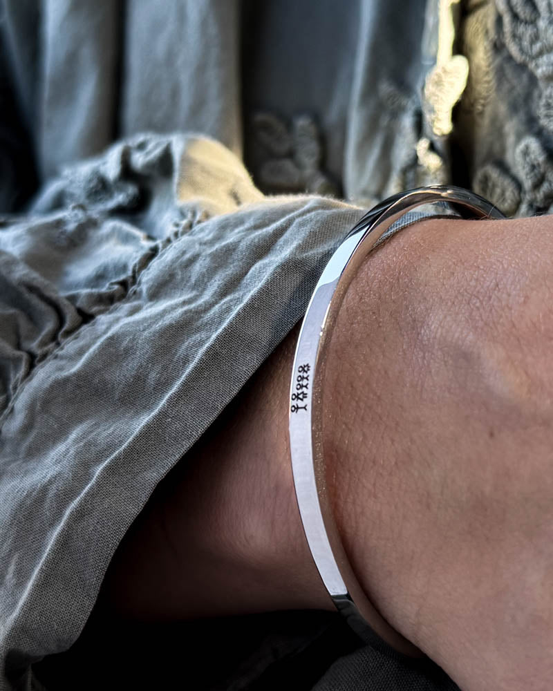 VENUS STICK bracelet in silver-coloured stainless steel with engraved matchstick family, worn with a grey puff-sleeve blouse