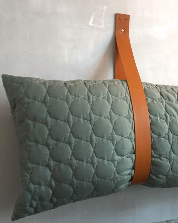 WAVE leather strap in cognac mounted on a wall as a holder for a green quilted cushion by a bench