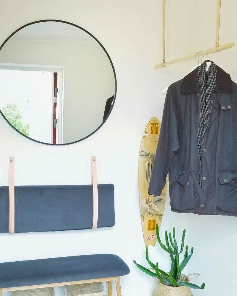 WAVE leather straps in natural hold a blue cushion as a backrest above a bench in a hallway with round mirror