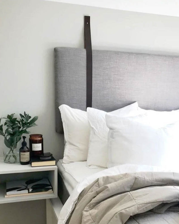 WAVE leather strap in black holds a grey upholstered headboard in a bright bedroom with white pillows