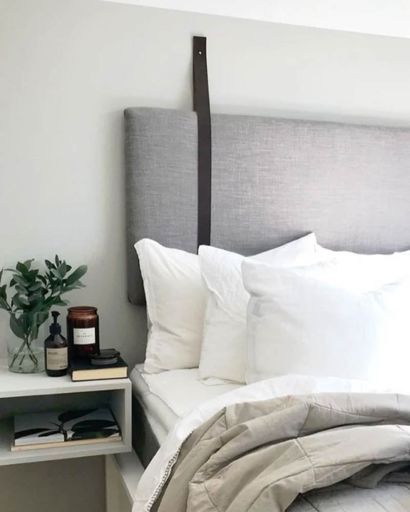 WAVE leather strap in black holds a grey upholstered headboard in a bright bedroom with white pillows