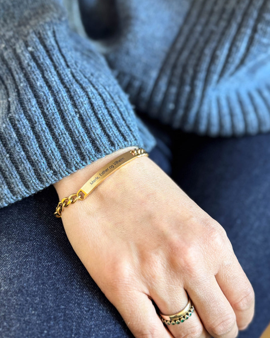 ZOE name bracelet in gold-plated stainless steel with "Merle, Esther og Vilhelm" engraved, on the wrist, blue knit and jeans