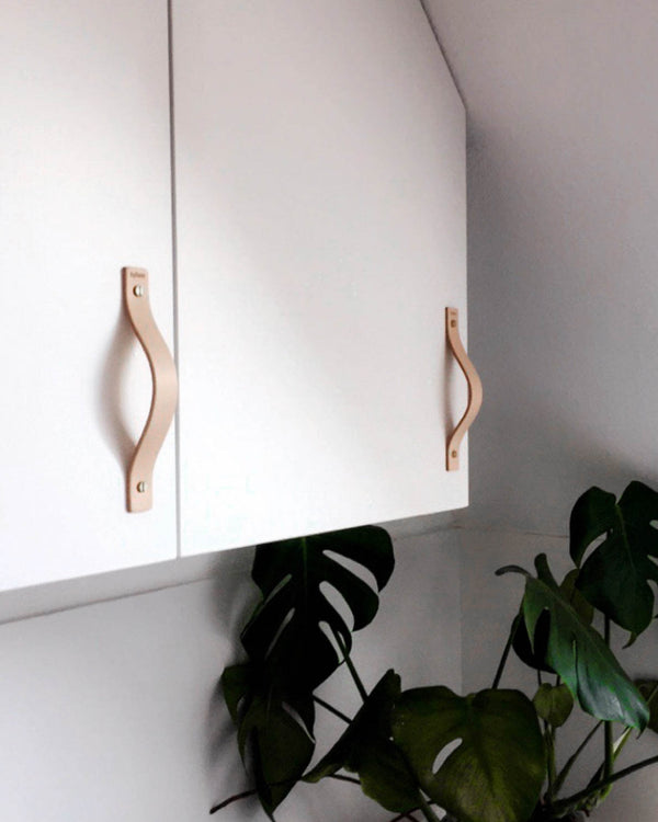 BAND leather handles in natural fitted on white wall cabinets with a monstera plant below